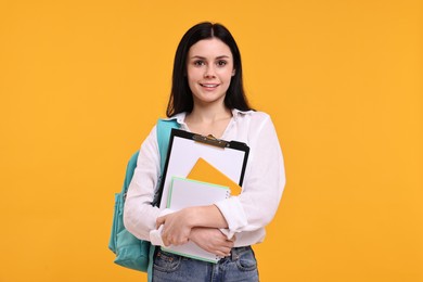 Photo of Smiling student with notebooks and clipboard on yellow background