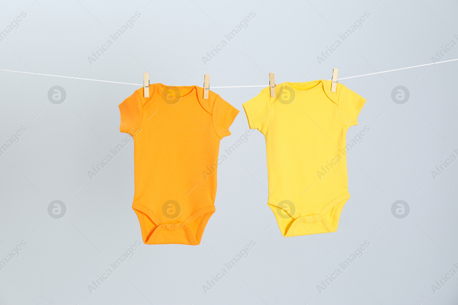 Photo of Different baby onesies hanging on clothes line against light grey background. Laundry day