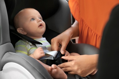 Photo of Mother fastening baby to child safety seat inside of car