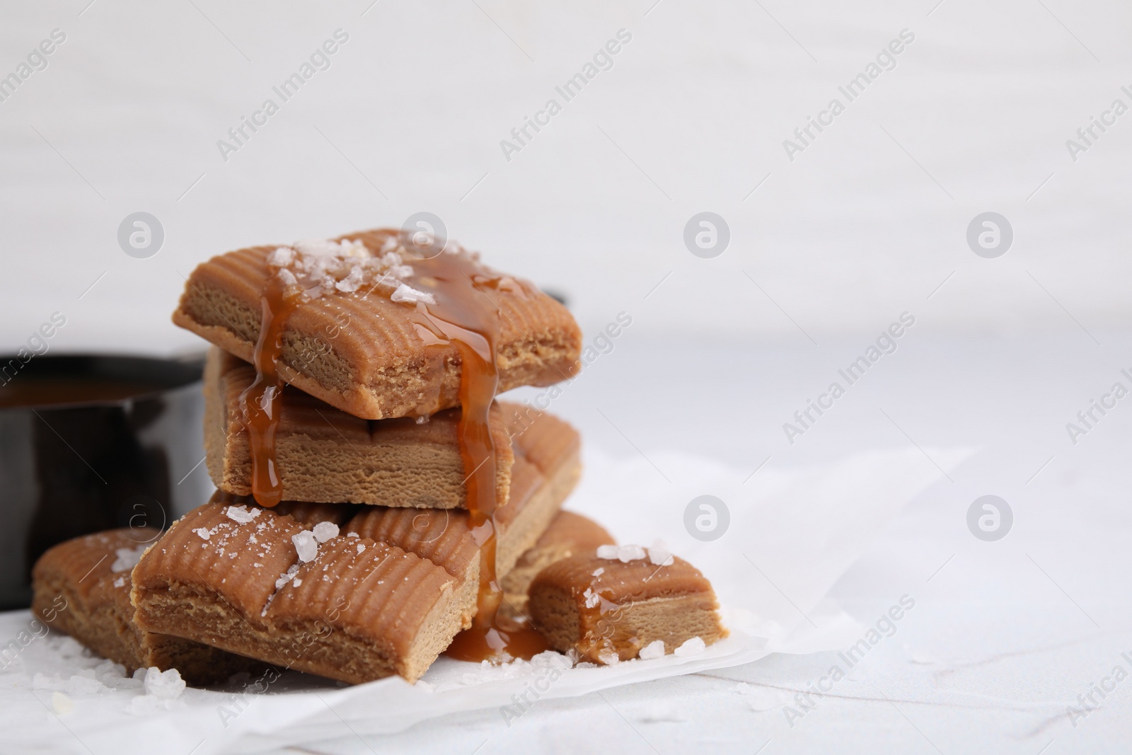 Photo of Yummy caramel candies, sauce and sea salt on white table, closeup. Space for text