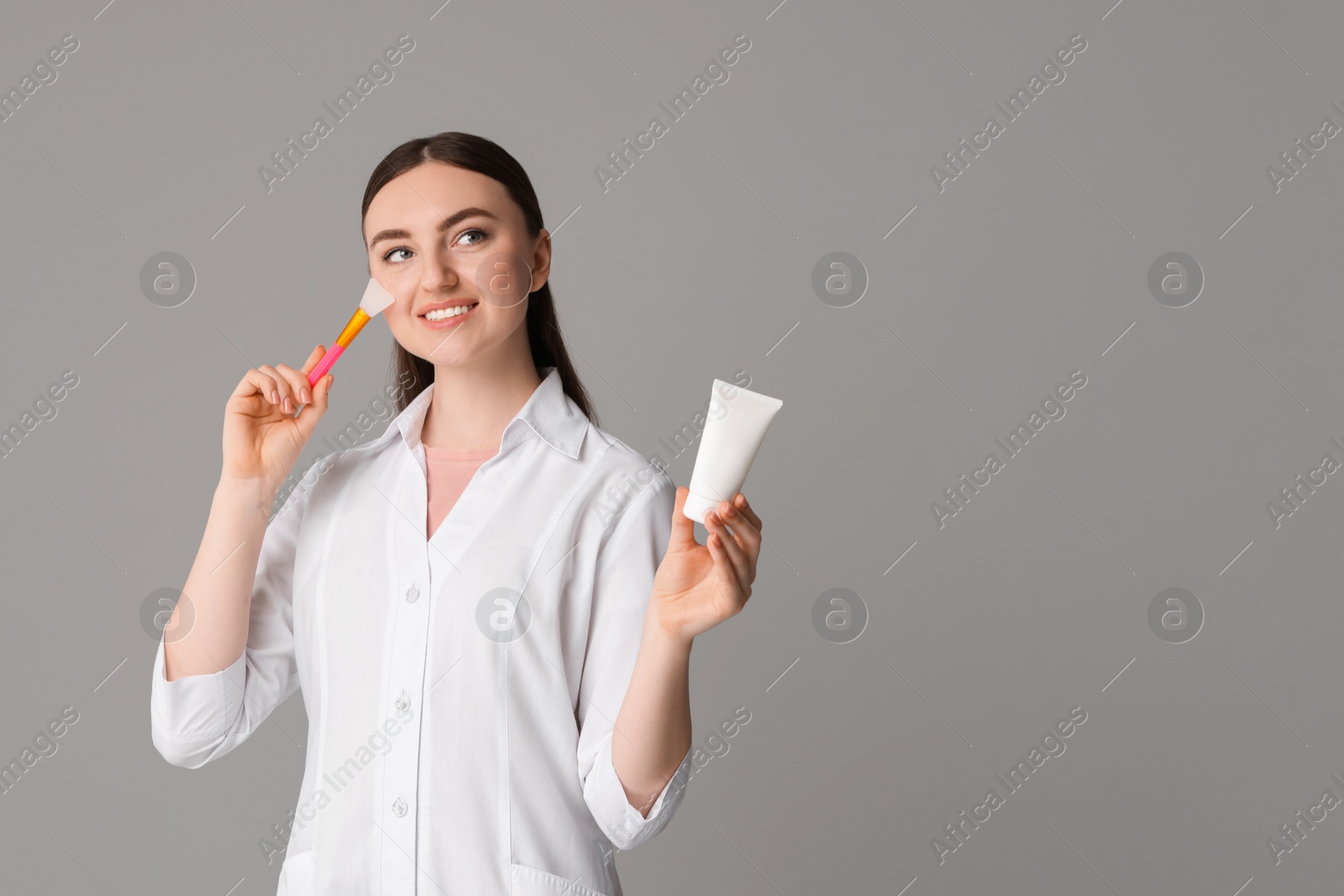 Photo of Cosmetologist with cosmetic product and silicone brush on grey background, space for text