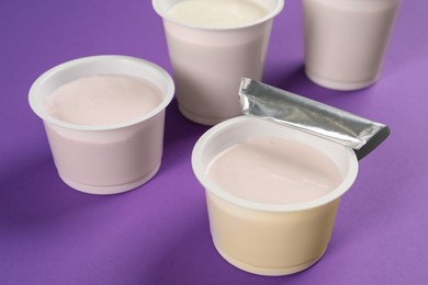 Plastic cups with tasty yogurt on purple background