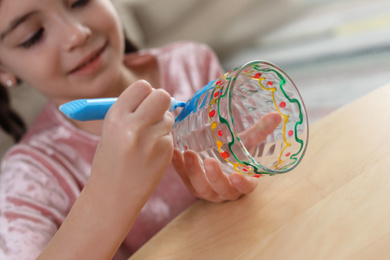 Photo of Little girl painting glass at table indoors, focus on hands. Creative hobby