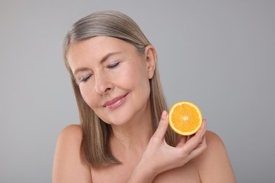 Beautiful woman with half of orange rich in vitamin C on grey background