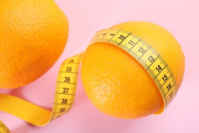 Cellulite problem. Oranges and measuring tape on pink background, closeup