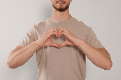Photo of Happy volunteer making heart with his hands on light background, closeup