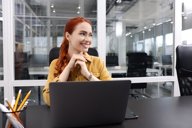 Photo of Happy woman working with laptop at black desk in office