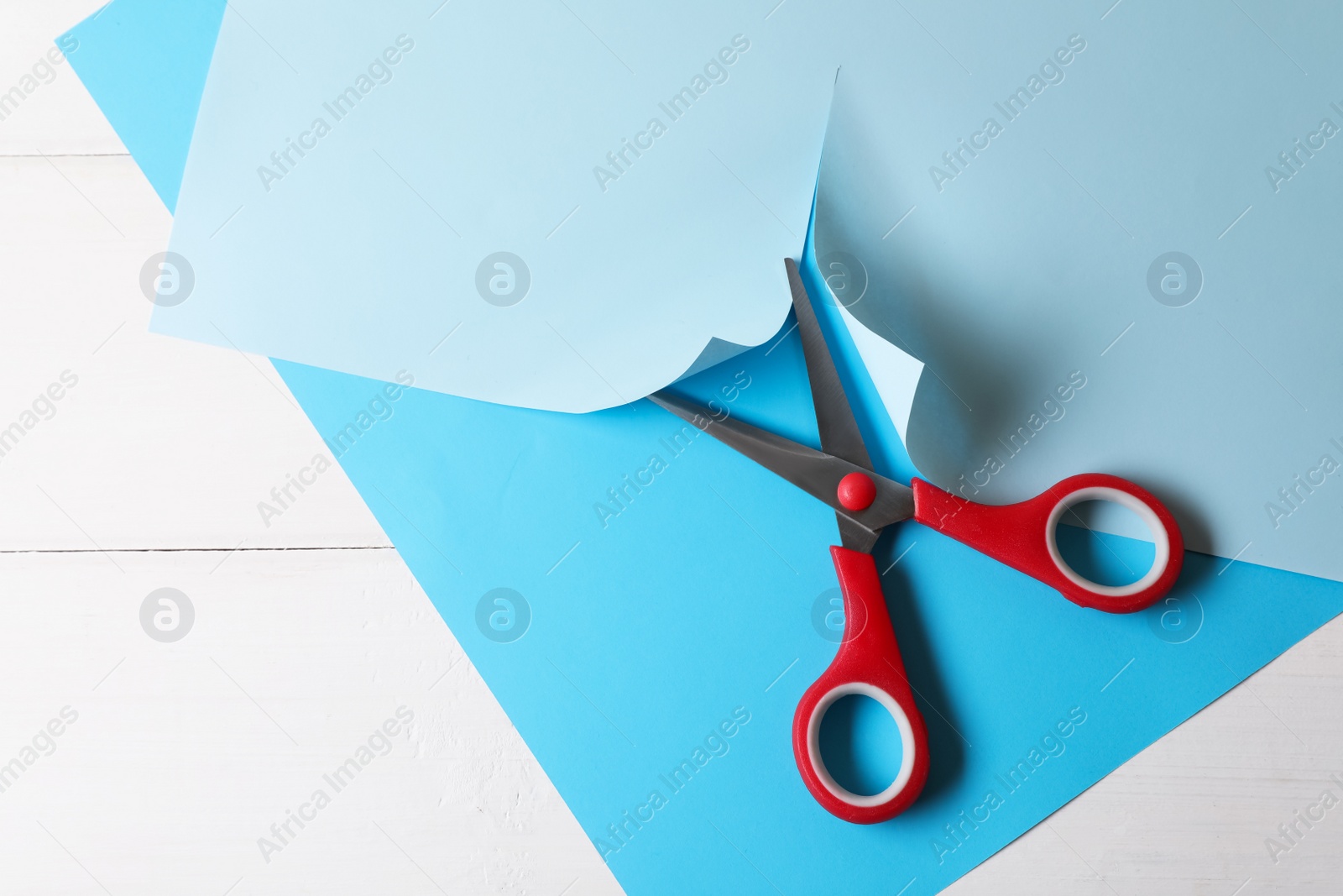 Photo of Red scissors and light blue paper on white wooden background, top view