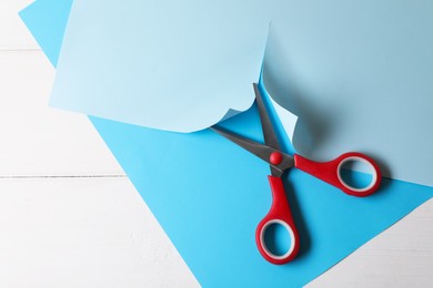 Photo of Red scissors and light blue paper on white wooden background, top view