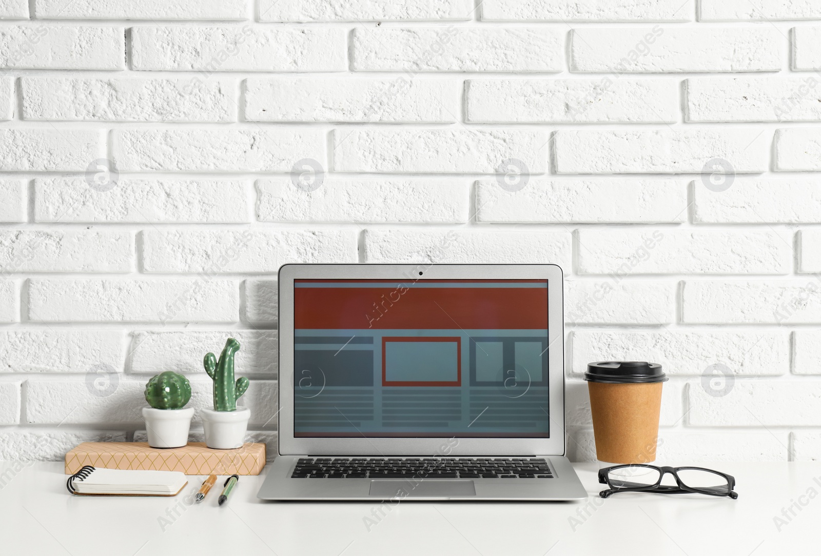 Photo of Modern workplace with laptop on table near brick wall. Space for design