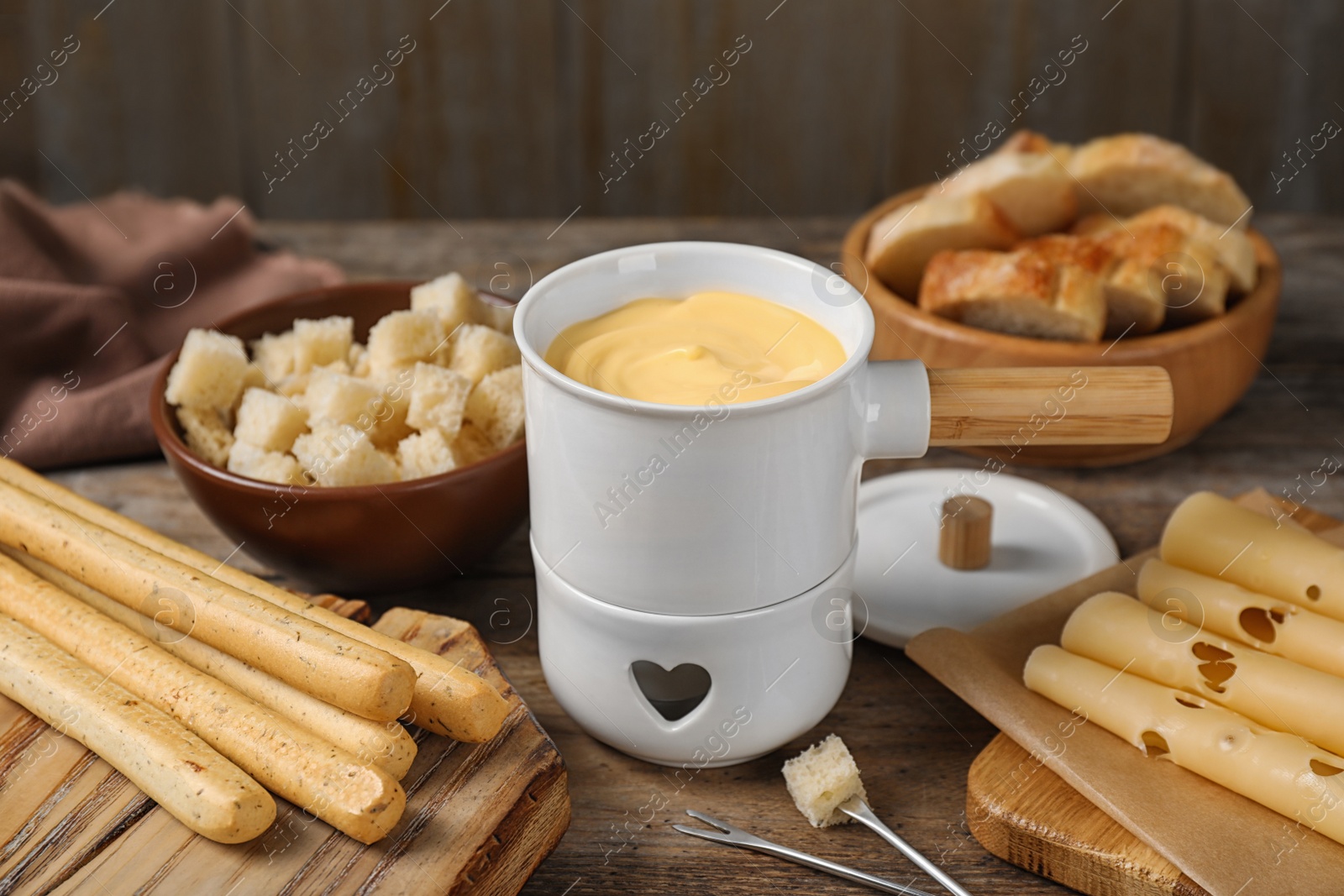 Photo of Pot of tasty cheese fondue with bread on wooden table