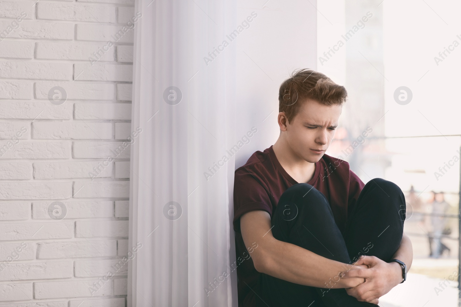 Photo of Upset teenage boy sitting alone near window indoors