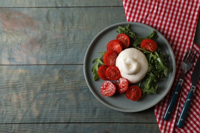 Photo of Delicious burrata cheese with tomatoes and arugula served on grey wooden table, flat lay. Space for text