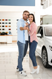 Photo of Happy couple with car key in modern auto dealership