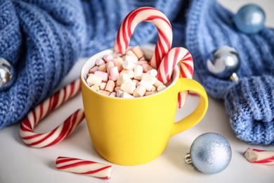 Photo of Cup of tasty cocoa with marshmallows, candy canes and Christmas decor on white table
