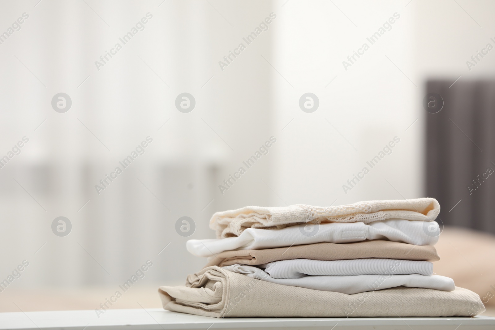 Photo of Stack of different folded clothes on white table indoors, closeup. Space for text