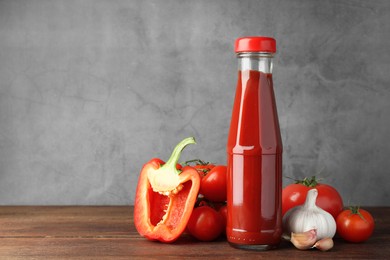 Photo of Bottle of tasty ketchup and ingredients on wooden table. Space for text
