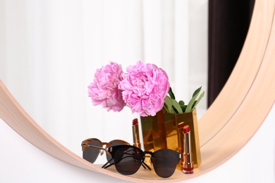 Photo of Stylish round mirror with sunglasses and flower on white wall indoors. Interior design