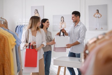 Photo of Shop assistant giving bags with clothes to customers in modern boutique