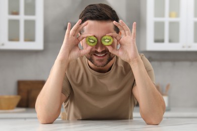 Photo of Man covering his eyes with halves of kiwi in kitchen