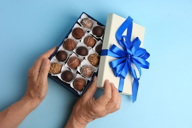Photo of Woman with box of delicious chocolate candies on light blue background, top view