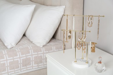 Photo of Holder with set of luxurious jewelry and perfume on nightstand in bedroom, space for text