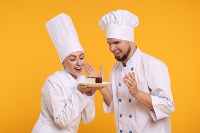 Photo of Happy professional confectioners in uniforms holding delicious cheesecake on yellow background