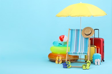 Photo of Deck chair, umbrella, suitcases and beach accessories on light blue background, space for text. Summer vacation