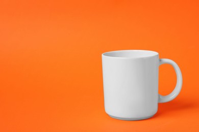 Photo of One white ceramic mug on orange background, space for text