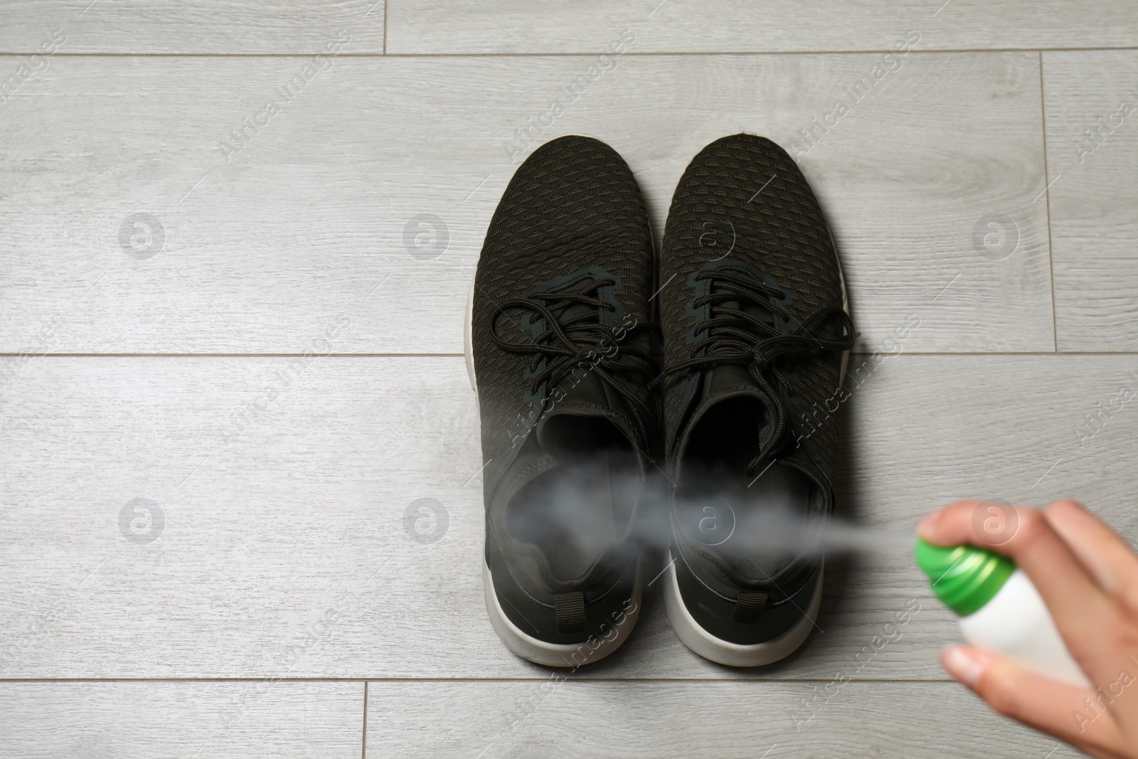 Image of Woman spraying deodorant over pair of shoes at home, closeup. Space for text
