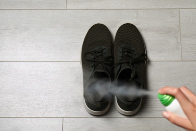 Image of Woman spraying deodorant over pair of shoes at home, closeup. Space for text