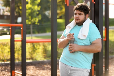 Photo of Young overweight man with bottle and towel on sports ground