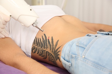 Photo of Young woman undergoing laser tattoo removal procedure in salon, closeup