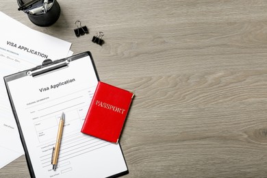 Photo of Visa application form, passport and stationery on wooden table, flat lay. Space for text