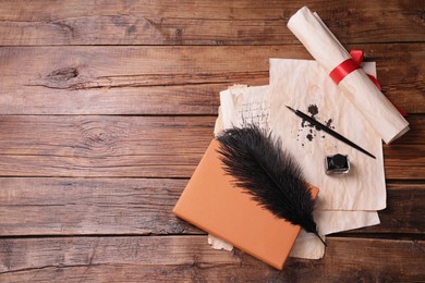 Photo of Black feather, inkwell, fountain pen and vintage parchment with ink stains on wooden table, flat lay. Space for text