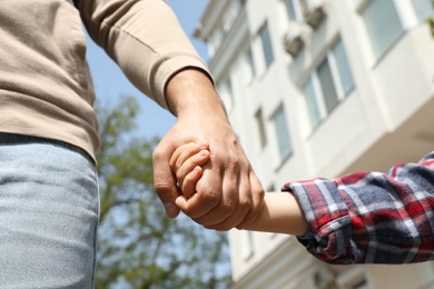 Photo of Little child holding hands with his father  outdoors, closeup. Family weekend