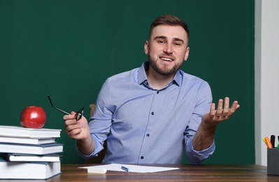Photo of Portrait of young teacher at table against green background