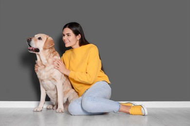 Photo of Happy woman with cute Labrador Retriever on floor against grey wall. Space for text
