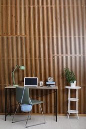 Photo of Stylish workplace interior with laptop on table near wooden wall. Space for text