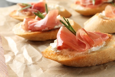 Photo of Tasty bruschettas with prosciutto and cream cheese on parchment, closeup. Space for text