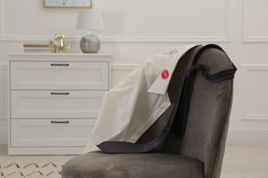 Photo of Men's shirt with lipstick kiss mark and necktie on sofa indoors