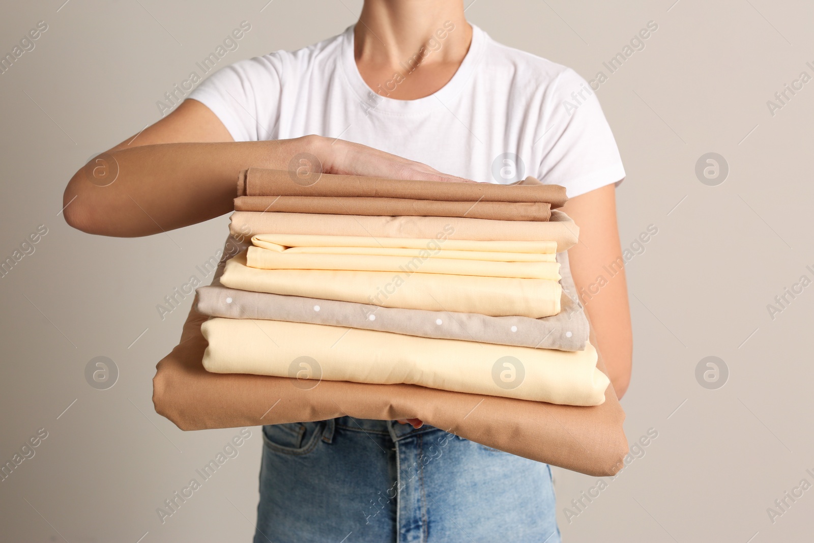 Photo of Woman holding stack of clean bed linens on beige background