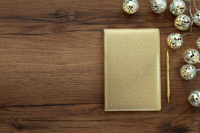 Photo of Golden planner, pen and Christmas lights on wooden table, flat lay. Space for text