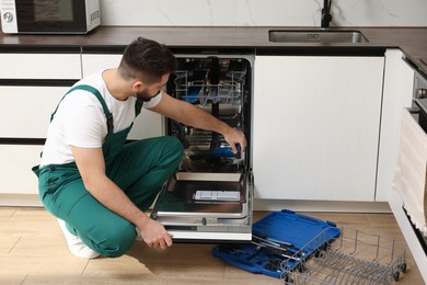 Photo of Serviceman repairing dishwasher door with screwdriver in kitchen