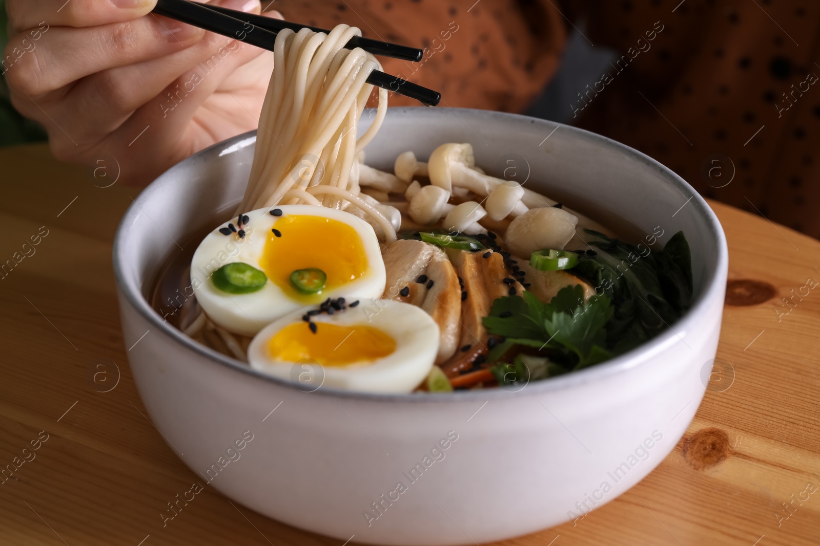 Woman eating delicious ramen with chopsticks at wooden table, closeup. Noodle soup Photo of Woman eating delicious ramen with chopsticks at wooden table, closeup. Noodle soup