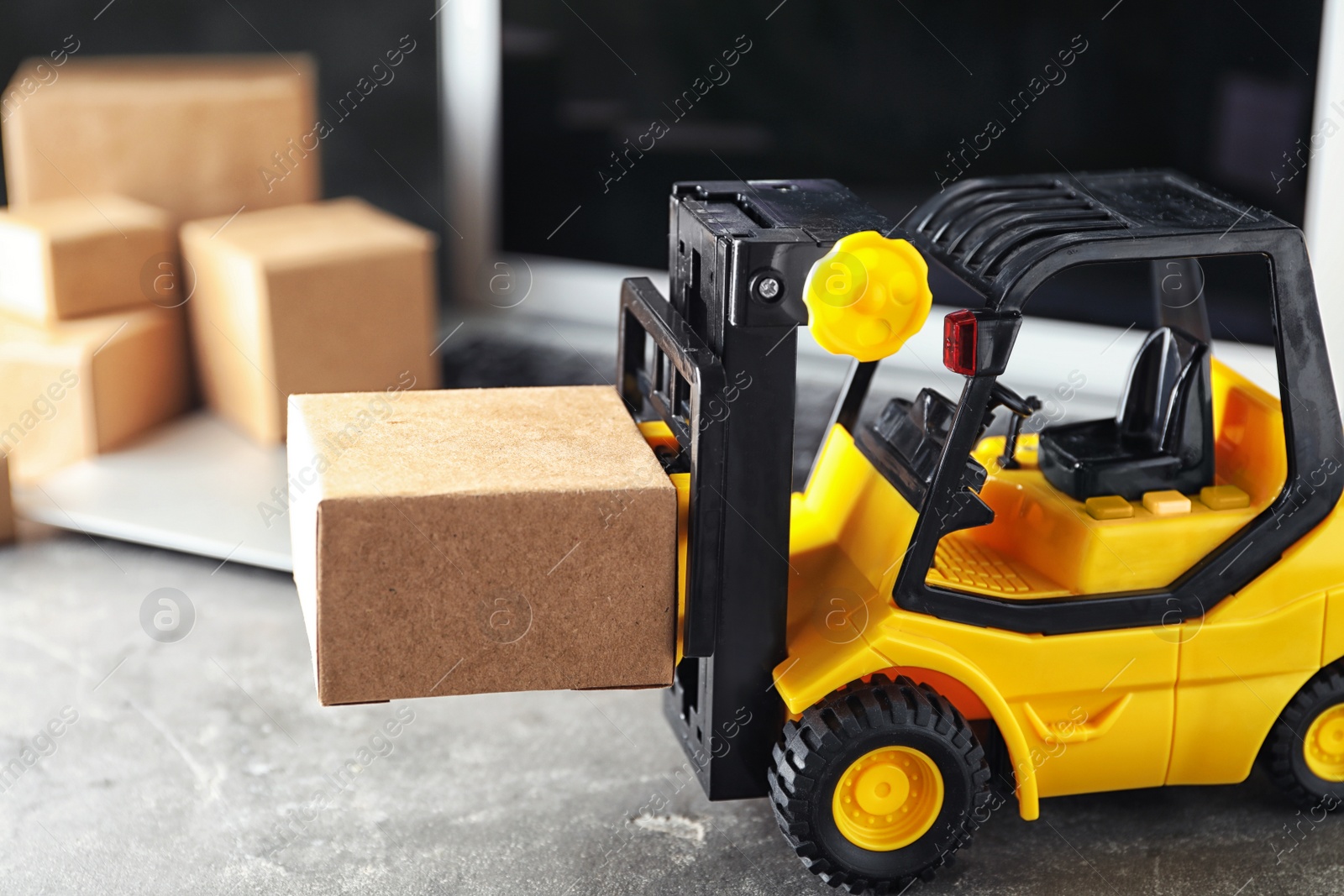 Photo of Toy forklift with box near laptop on table. Logistics and wholesale concept