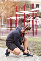 Photo of Young man with headphones tying shoelaces on sports ground