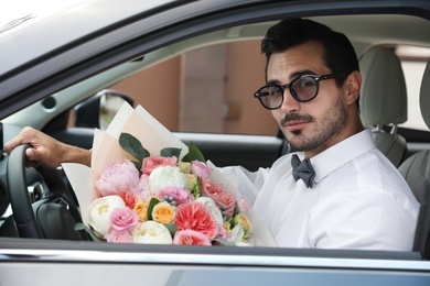 Photo of Young handsome man with beautiful flower bouquet sitting in car