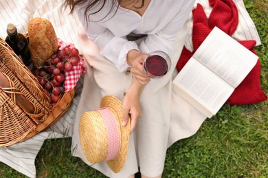 Photo of Woman with glass of wine, book and picnic basket on green grass, above view