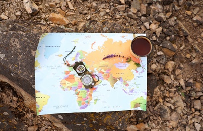 Photo of Compass, mug with drink and map on rock outdoors, top view. Camping season